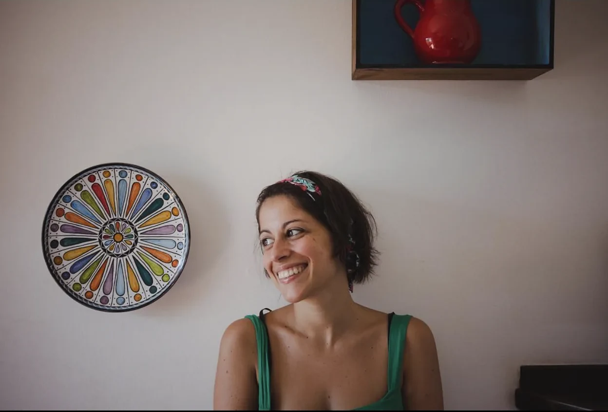 Tiziana sorride accanto a un piatto decorato appeso al muro